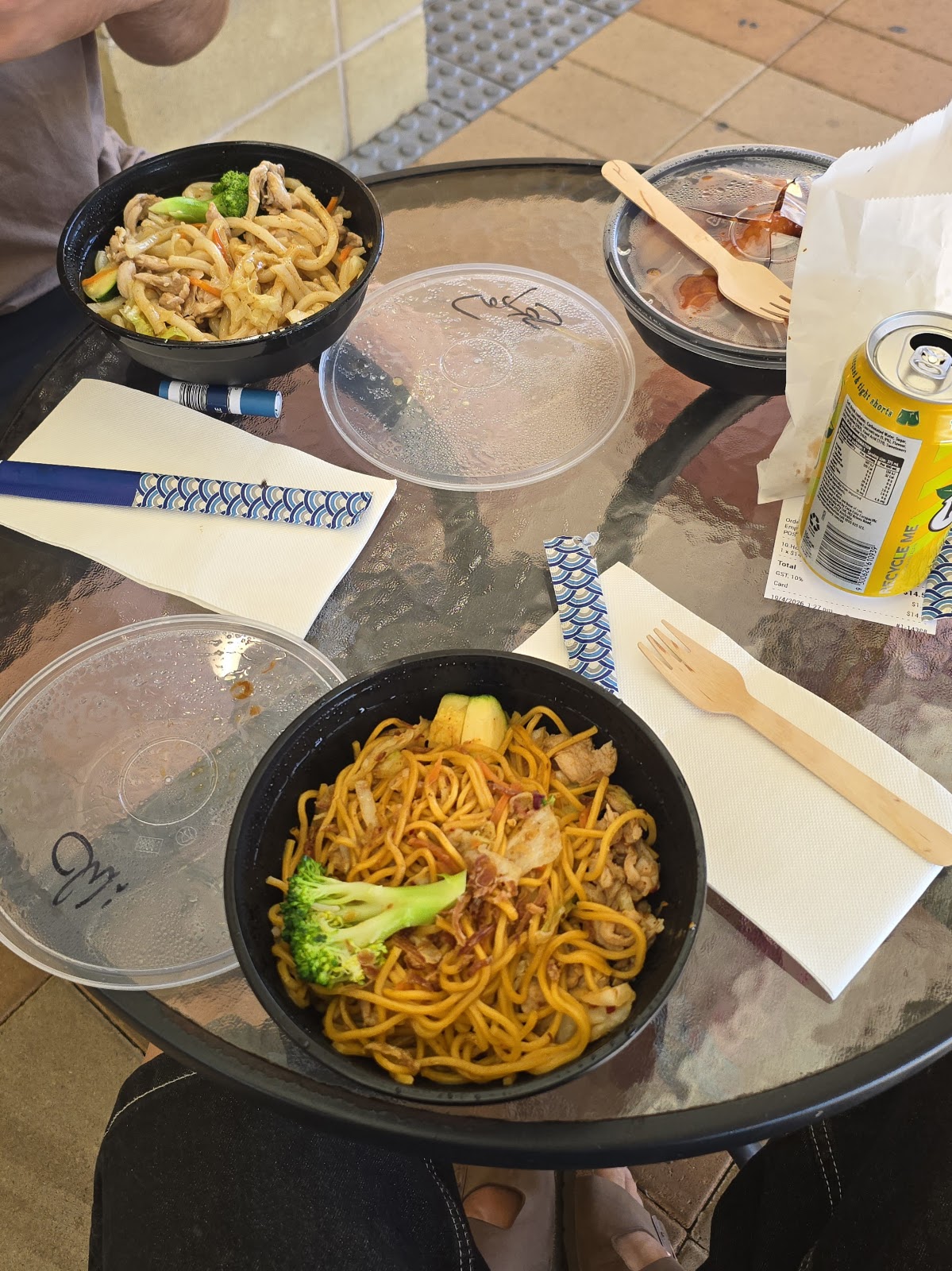 Two bowls of stir-fried noodles with broccoli, served at an outdoor table