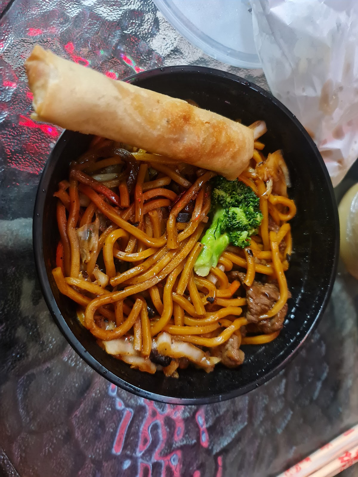 Stir-fried egg noodles with a spring roll across the bowl